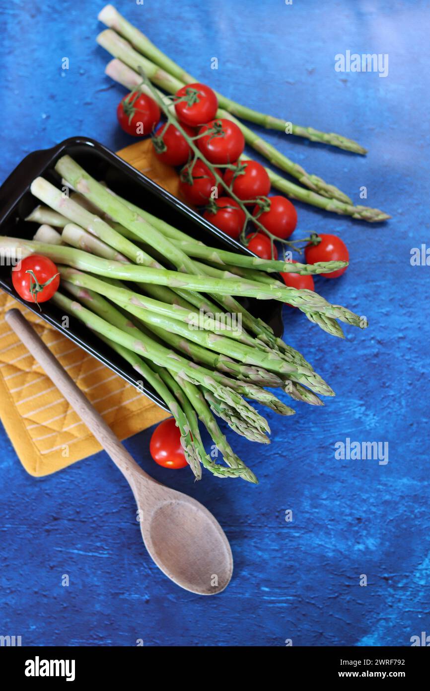 Fresh green asparagus with cherry tomatoes and sea salt on blue background Stock Photo