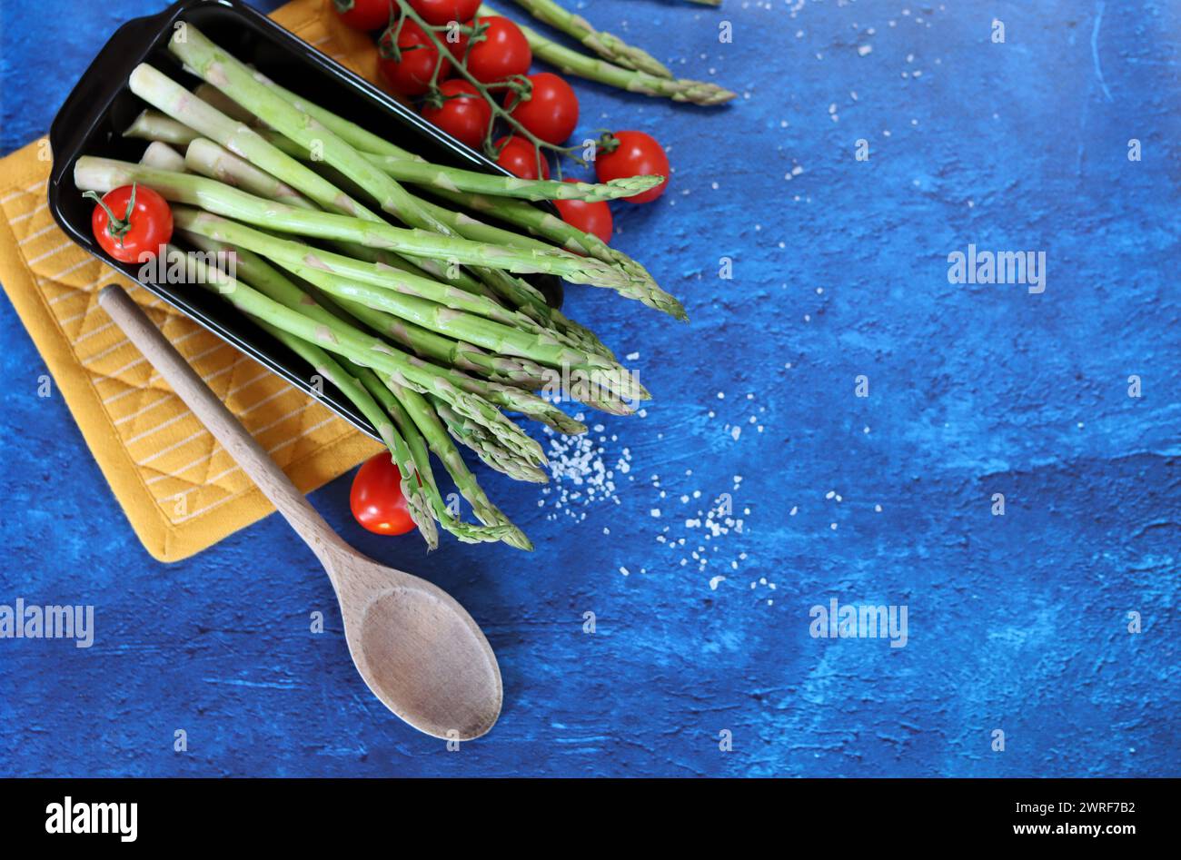 Fresh green asparagus and cherry tomatoes on blue textured background with copy space. healthy dinner preparation. Balanced diet concept. Stock Photo