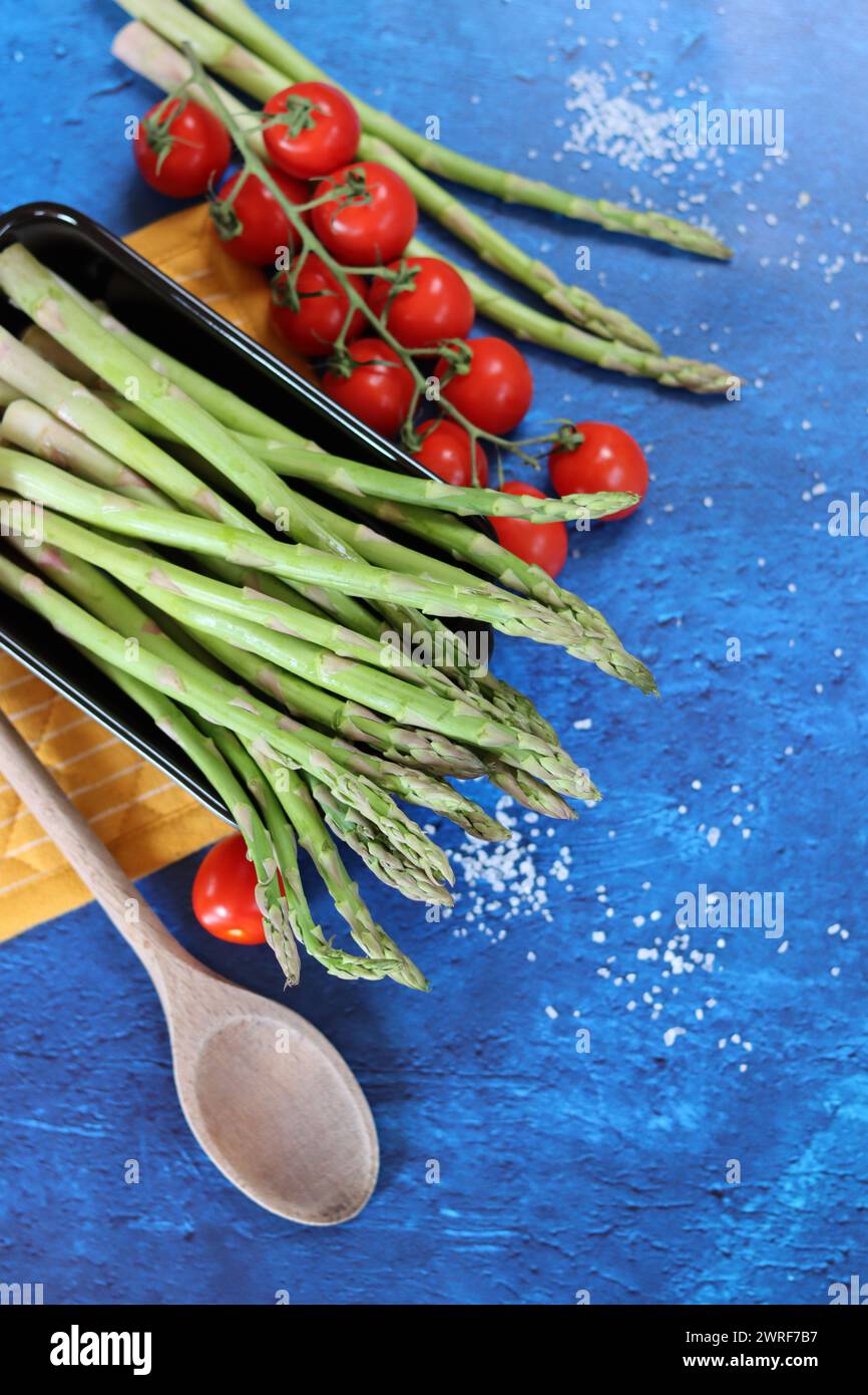 Fresh green asparagus and cherry tomatoes on blue textured background with copy space. healthy dinner preparation. Balanced diet concept. Stock Photo