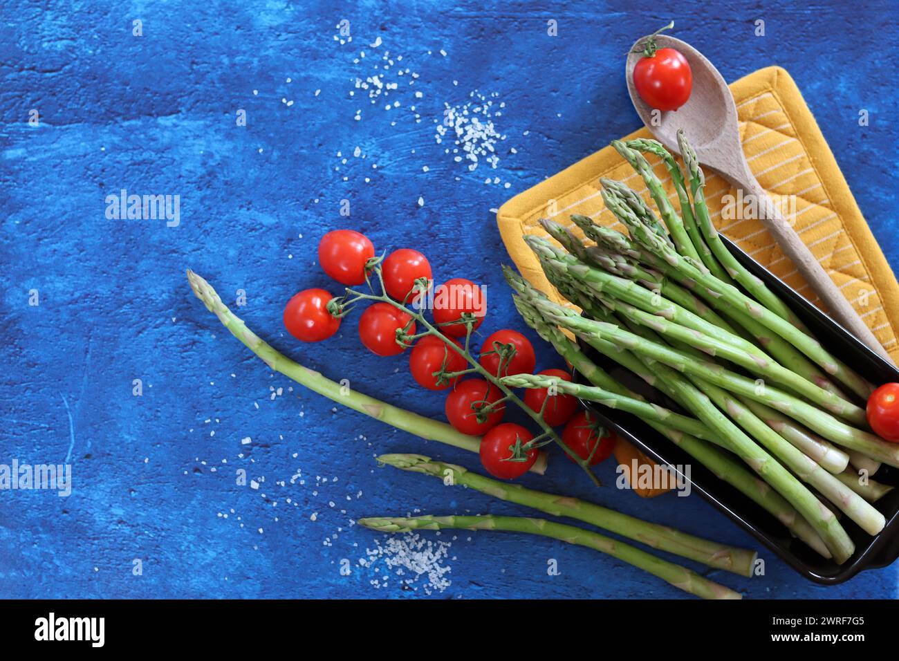 Fresh green asparagus and cherry tomatoes on blue textured background with copy space. healthy dinner preparation. Balanced diet concept. Stock Photo