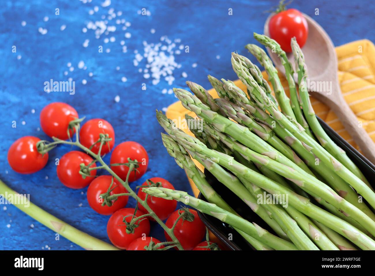 Fresh green asparagus with cherry tomatoes and sea salt on blue background Stock Photo