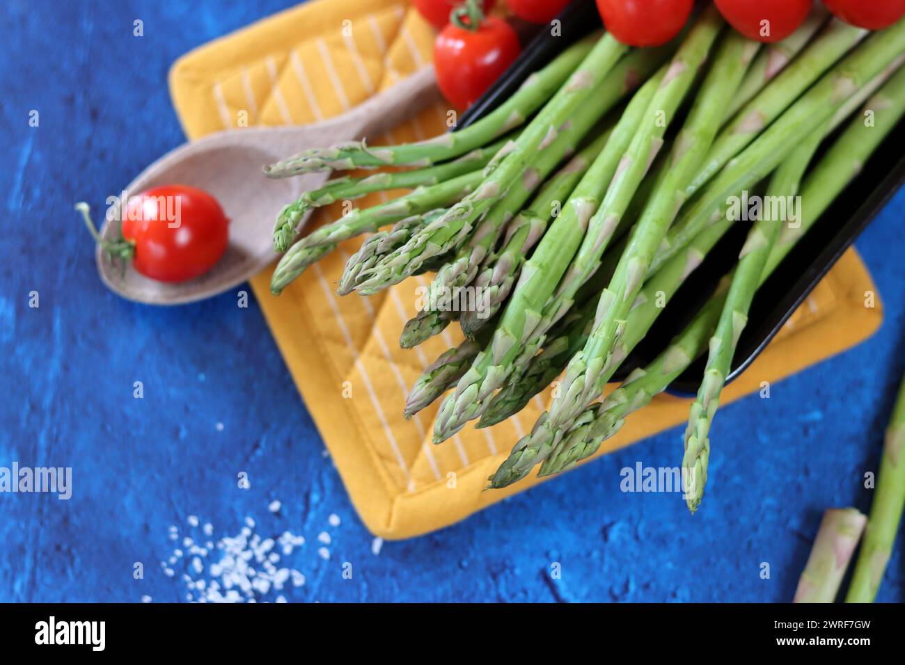 Fresh green asparagus and cherry tomatoes on blue textured background with copy space. healthy dinner preparation. Balanced diet concept. Stock Photo