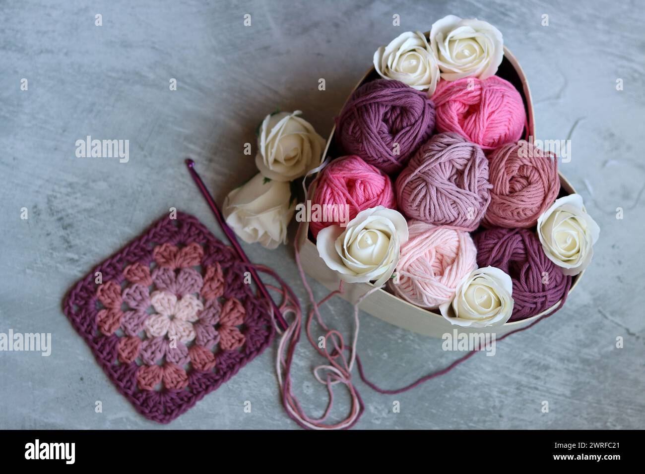 Heart-shaped box with white roses and cotton yarn on a gray background. Cotton yarn texture close up photo. Art and craft concept. Stock Photo