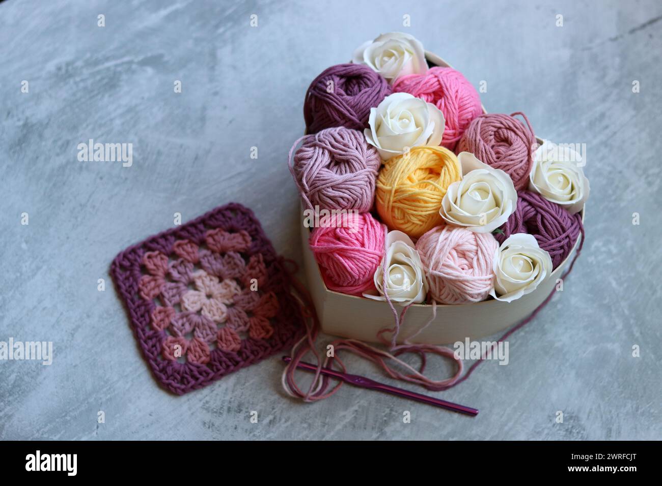 Heart-shaped box with white roses and cotton yarn on a gray background. Cotton yarn texture close up photo. Art and craft concept. Stock Photo