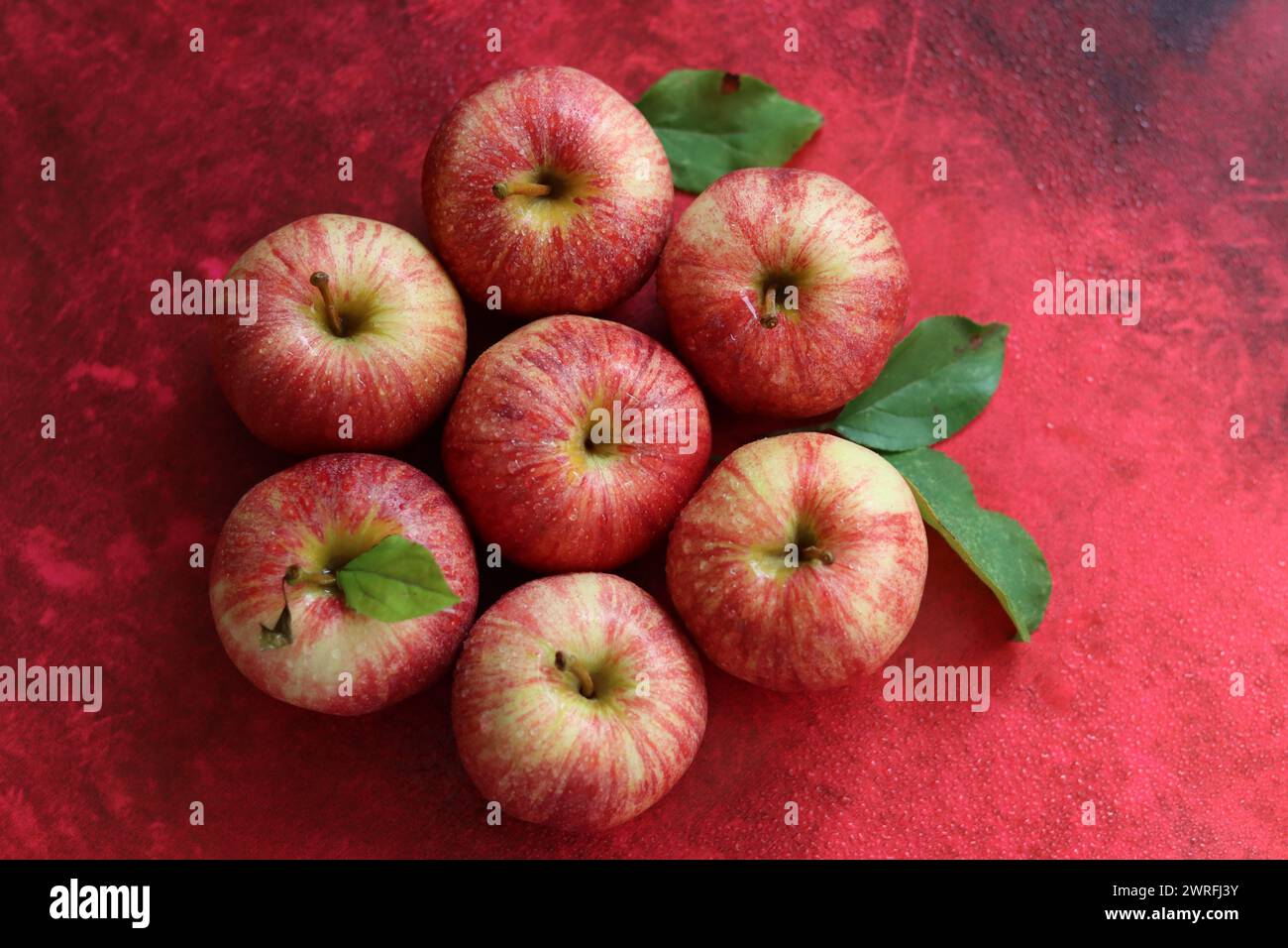 Red apples with leaves on red background. Top view, flat lay Stock Photo