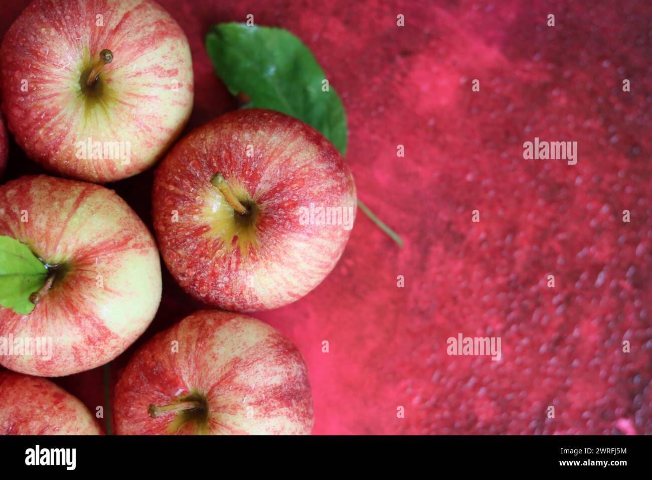 Red apples with leaves on red background. Top view, flat lay Stock Photo