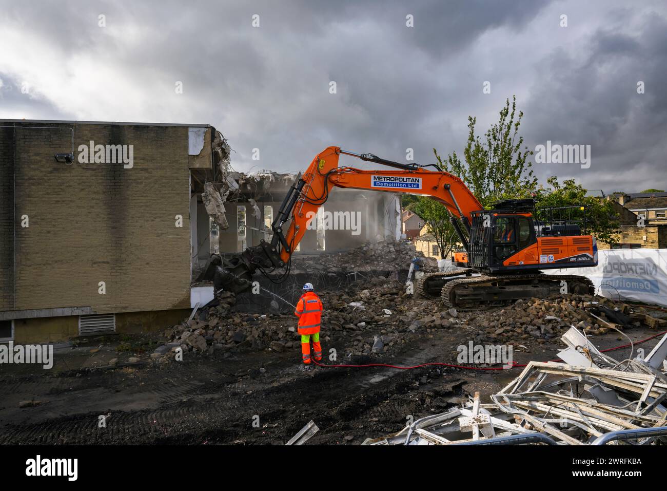 Demolition site (man in hi-vis working hosing rubble, building deconstruction, controlled collapse, empty shell) - Baildon, West Yorkshire England UK. Stock Photo