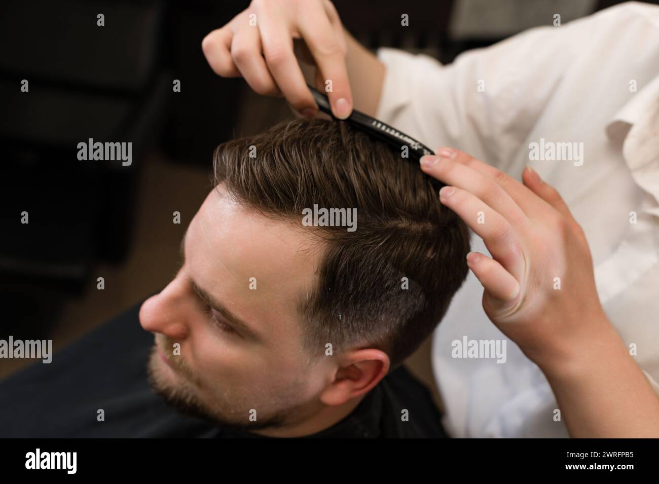 Hair styling with a comb, combing the client's hair by a stylist. Haircut of a visitor in a barbershop. Stock Photo