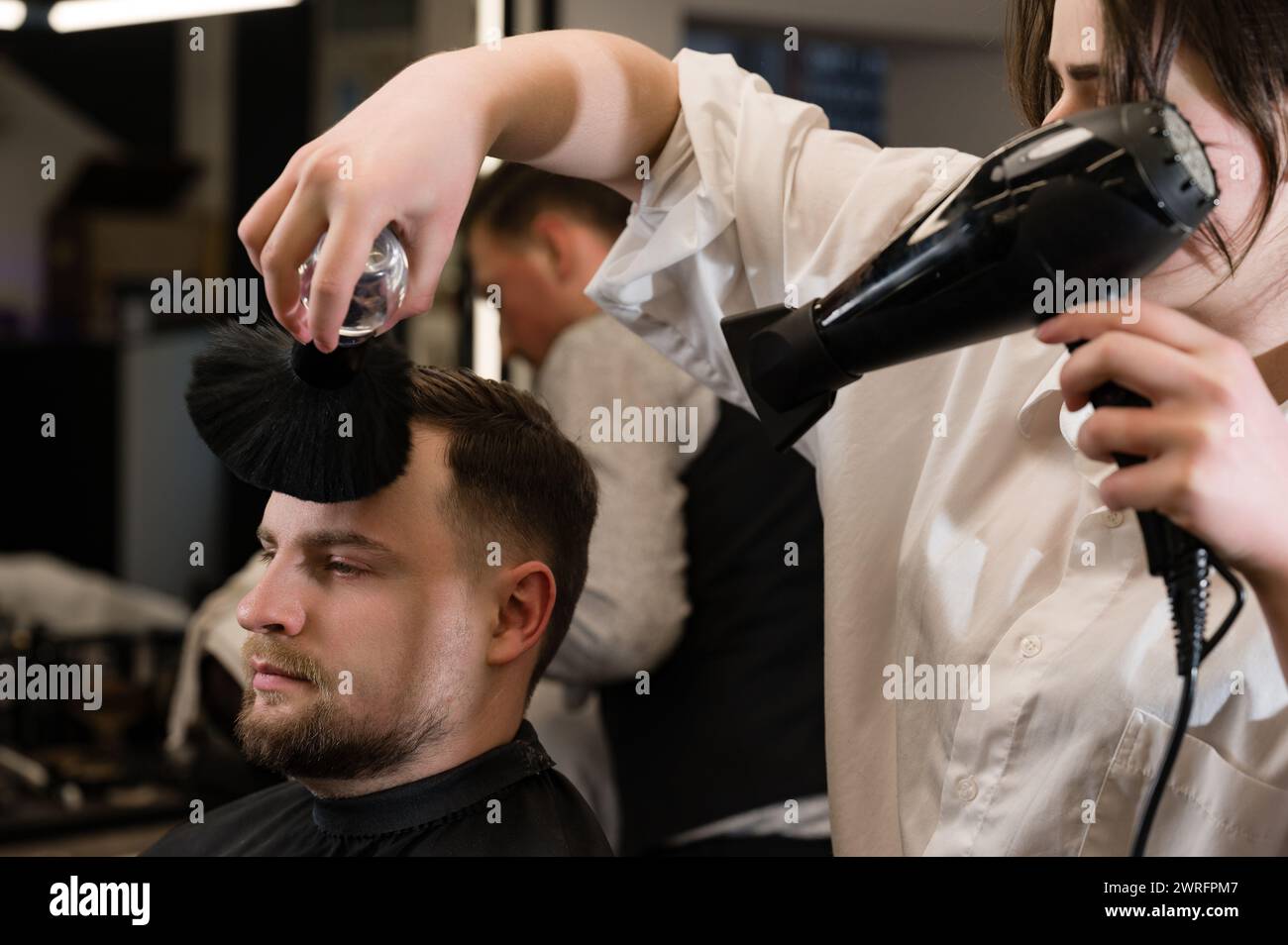 The hairdresser sweeps the hair during the haircut with a brush and cold drying air. Stock Photo