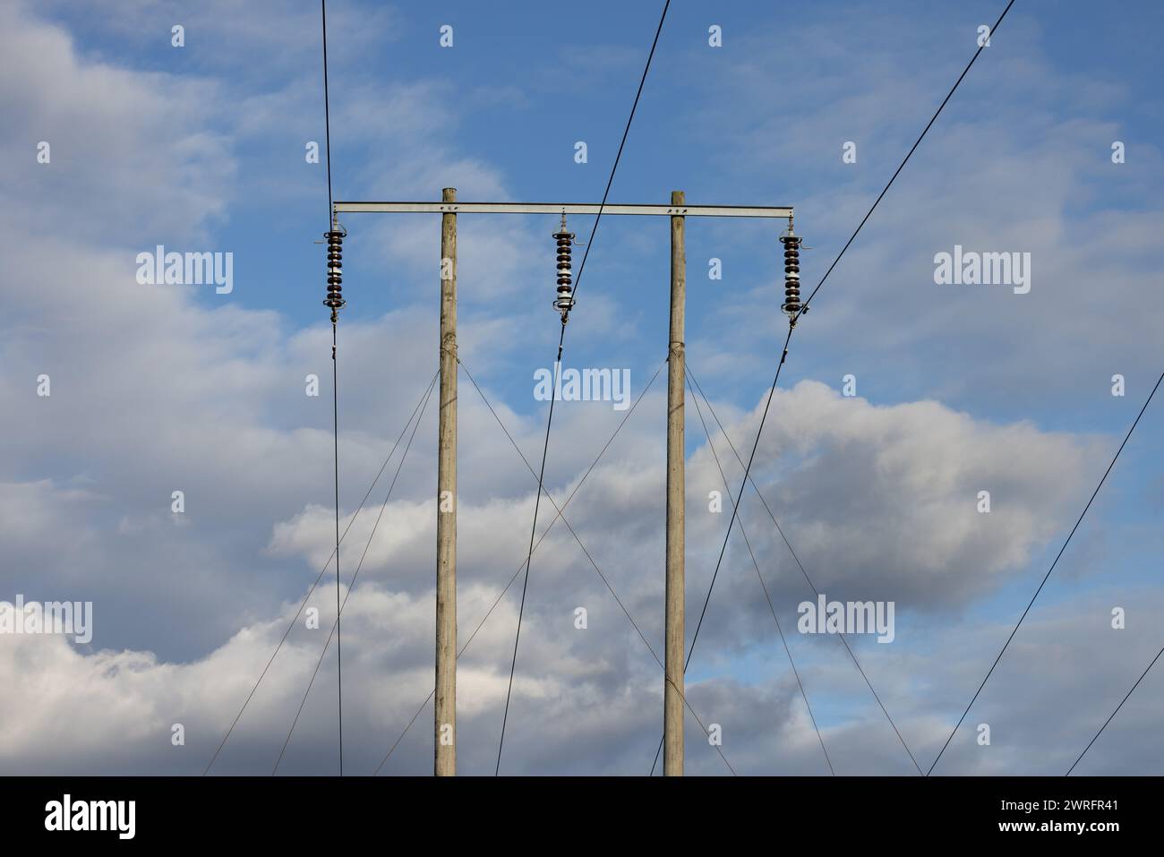 Electrical wooden pylon, cables and isolators against sky with mixed clouds Stock Photo