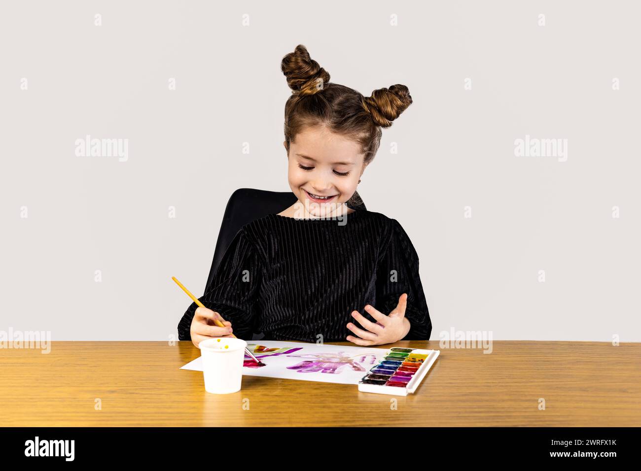 A little girl with a smile on her face is sitting at a hardwood table ...