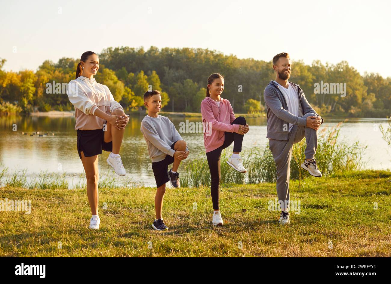 Fit and active happy parents with two kids boy and girl doing sport exercises in nature. Stock Photo