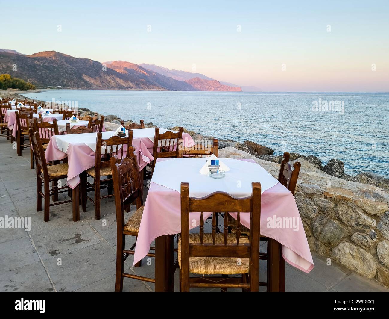 Outdoors traditional seaside taverna at Paleochora village, afternoon in Crete island Greece. Tavern restaurant, empty chair table, paved alley. Stock Photo