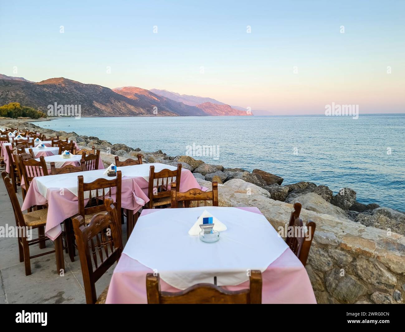 Outdoors traditional seaside taverna at Paleochora village, afternoon in Crete island Greece. Tavern restaurant, empty chair table, paved alley. Stock Photo