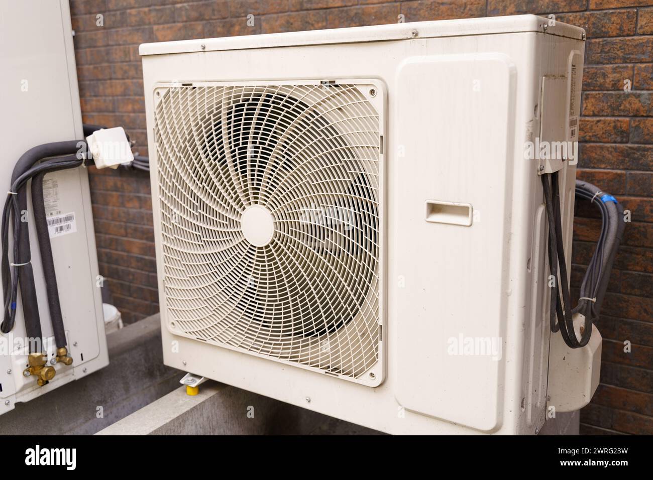 A white air conditioner unit positioned next to a weathered brick wall ...