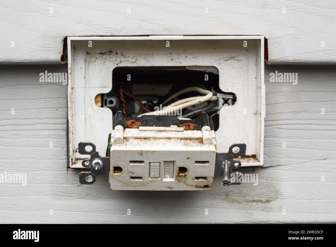 Weathered exterior electrical outlet hanging from attached wiring Stock