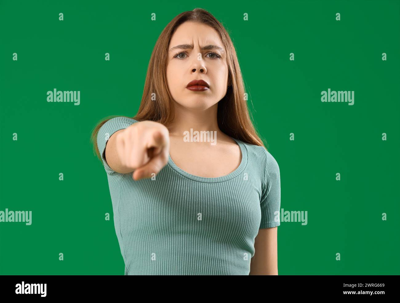 Young woman pointing at viewer on green background. Accusation concept ...