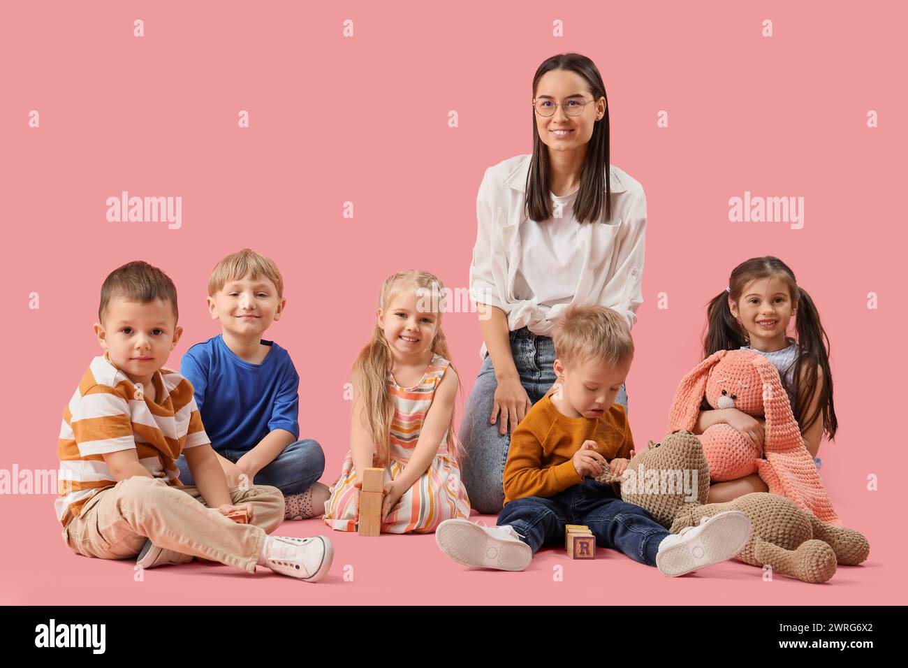 Little children with toys and nursery teacher on pink background Stock Photo