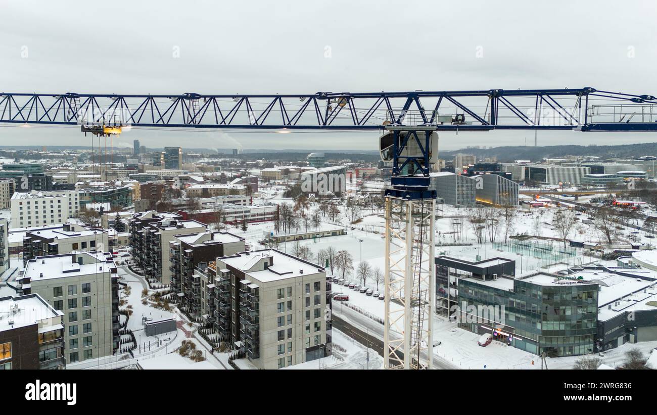 Drone photography of a metal crane and city landscape covered by snow during cloudy winter day Stock Photo