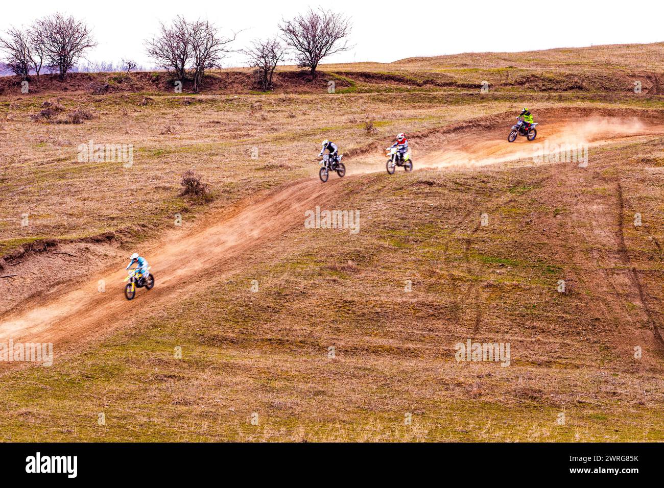 A group of people are riding dirt bikes on a dirt track in a grassy ...
