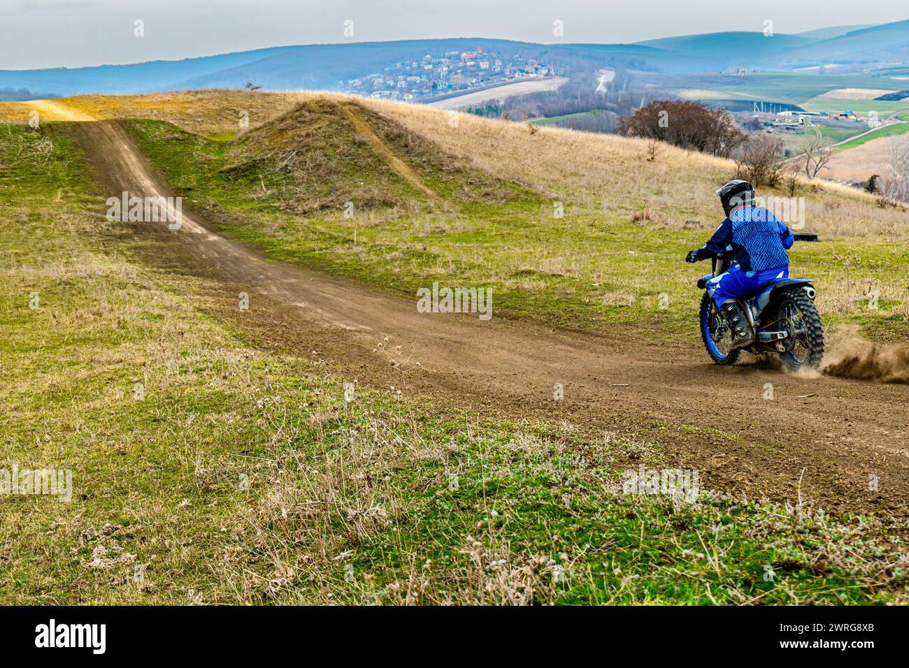 The individual is maneuvering a dirt bike on a dirt road, navigating through highlands with grassy slopes. They are wearing a helmet for safety while Stock Photo