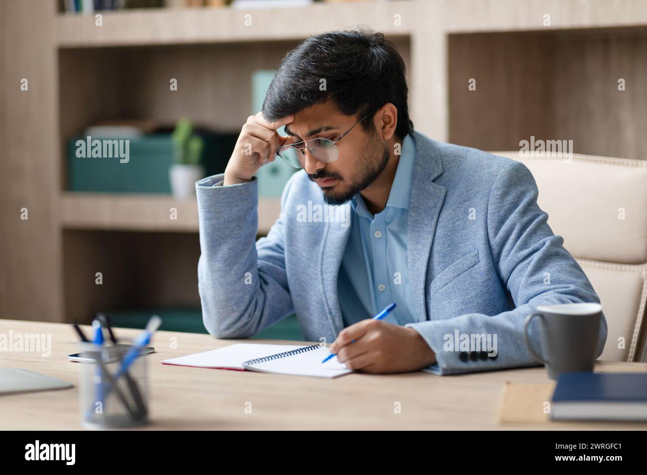 Indian entrepreneur man taking notes with concerned expression in office Stock Photo