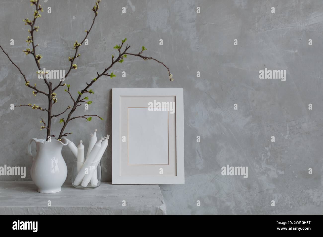 Blank picture frame next to cherry plum branches in a jug and candles on a mantelpiece Stock Photo