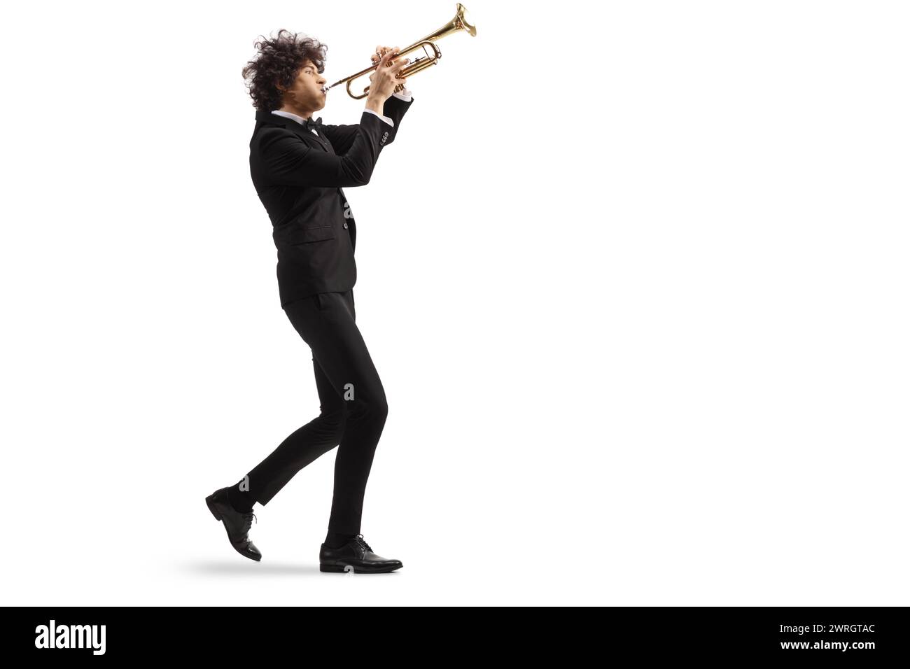 Male musician in a black suit walking and playing a trumpet isolated on white background Stock Photo