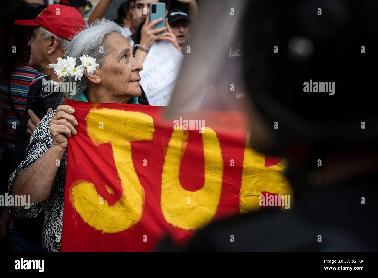 A pensioner with flowers in her hair holds a banner in front of the police cordon during the demonstration. The Omnibus Law of more than 600 articles presented by President Javier Milei brought dozens of hours of parliamentary debate, accompanied by several days of popular resistance in the streets surrounding the National Congress. These days were marked by the political thread, the negotiation, the back and forth, the protest and the repression. The year of 2024 in Buenos Aires, Argentina, began with tear gas, sticks, rubber bullets and laws that rose and fell back to committee. (Photo by Sa Stock Photo