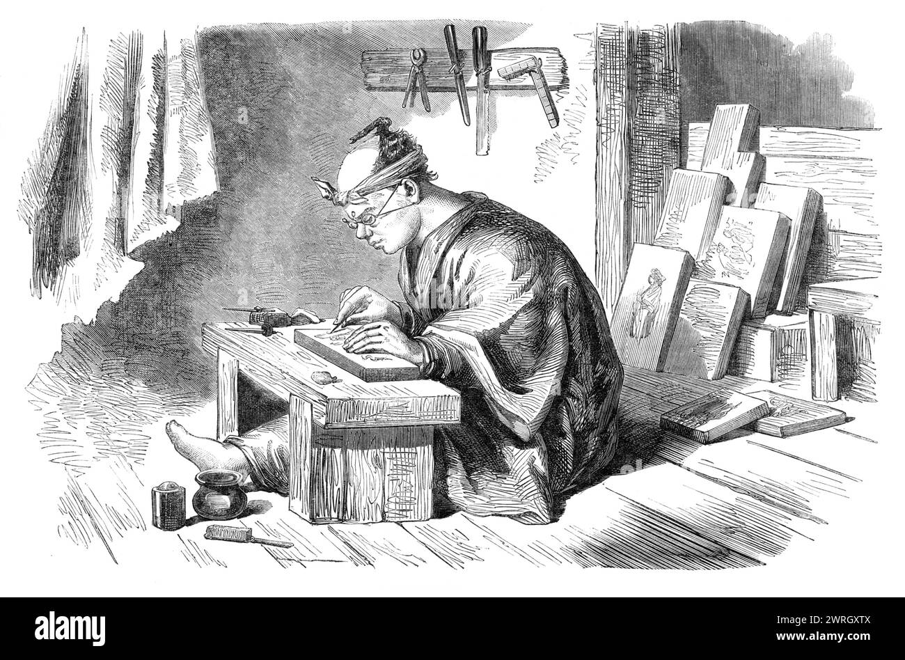 A Japanese wood-engraver, 1864. '...from a sketch by our Artist at Yokohama. It is painful here to observe the uncomfortable position of the Japanese engraver at his work - to see how he is doubled up at the apology for a table, and in what an awkward way he holds the style. But we are amused when we look at his wonderful spectacles, tied round his ears with a piece of string. The instruments he uses are of the simplest description; and his wood is not hard, like our boxwood, but extremely soft. His mode of operation is this: the subject to be engraved is first drawn on a thin piece of paper w Stock Photo