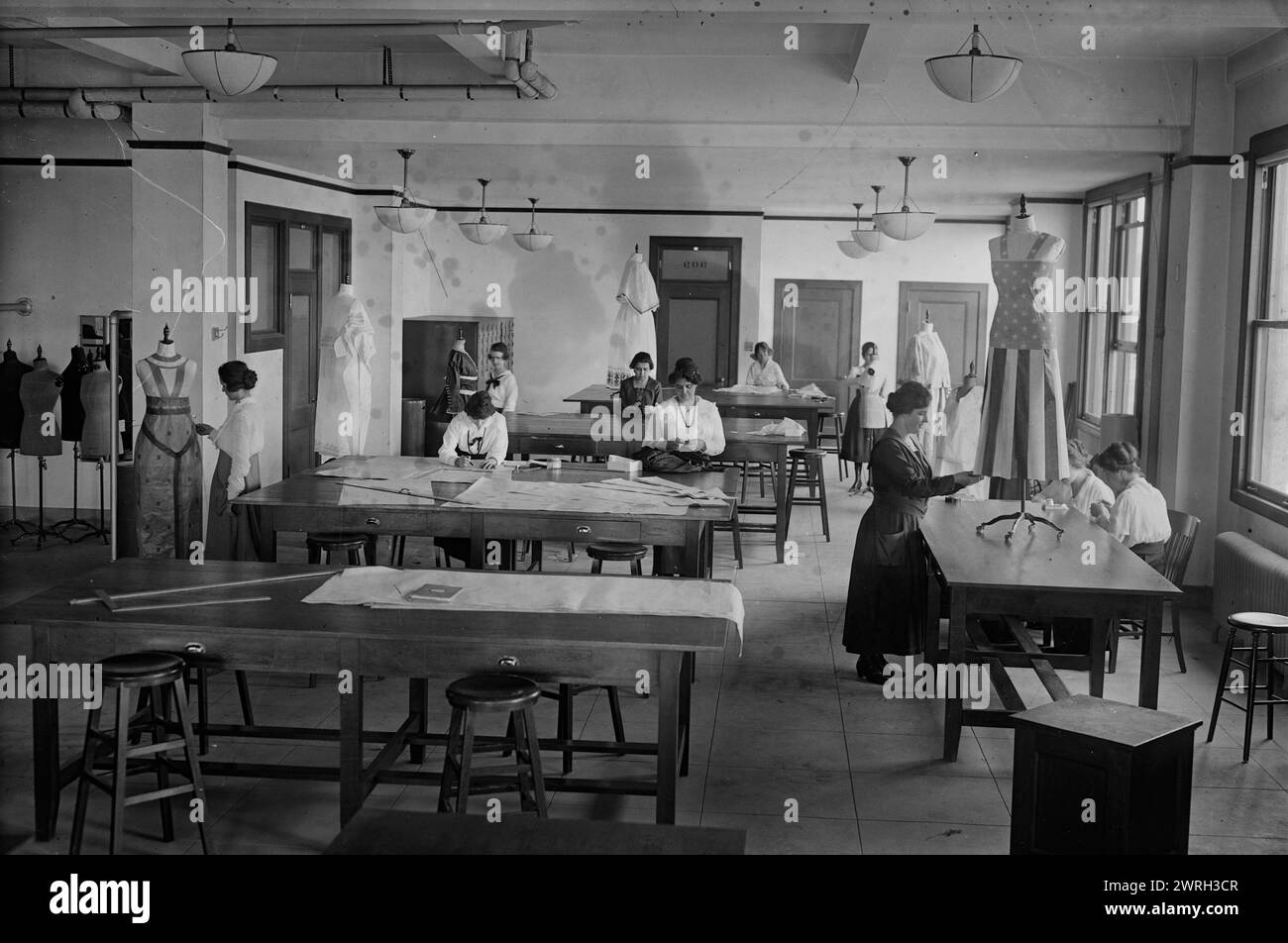 Y.W.C.A., between c1915 and 1918. Women making dresses at the Y.W.C.A during World War I. One dress has a striped skirt and star-patterned top which resembles an American flag. Stock Photo