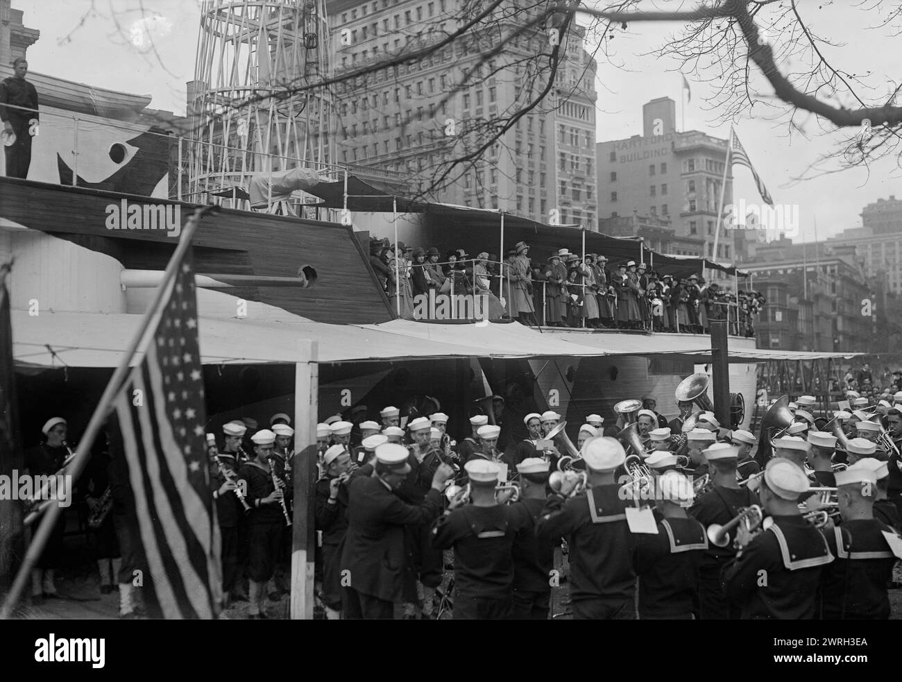 French women on RECRUIT, 1917 or 1918. A military band playing next to the USS Recruit, a wooden mockup of a battleship built in Union Square, New York City by the Navy to recruit seamen and sell Liberty Bonds during World War I. French women stand on deck. Stock Photo