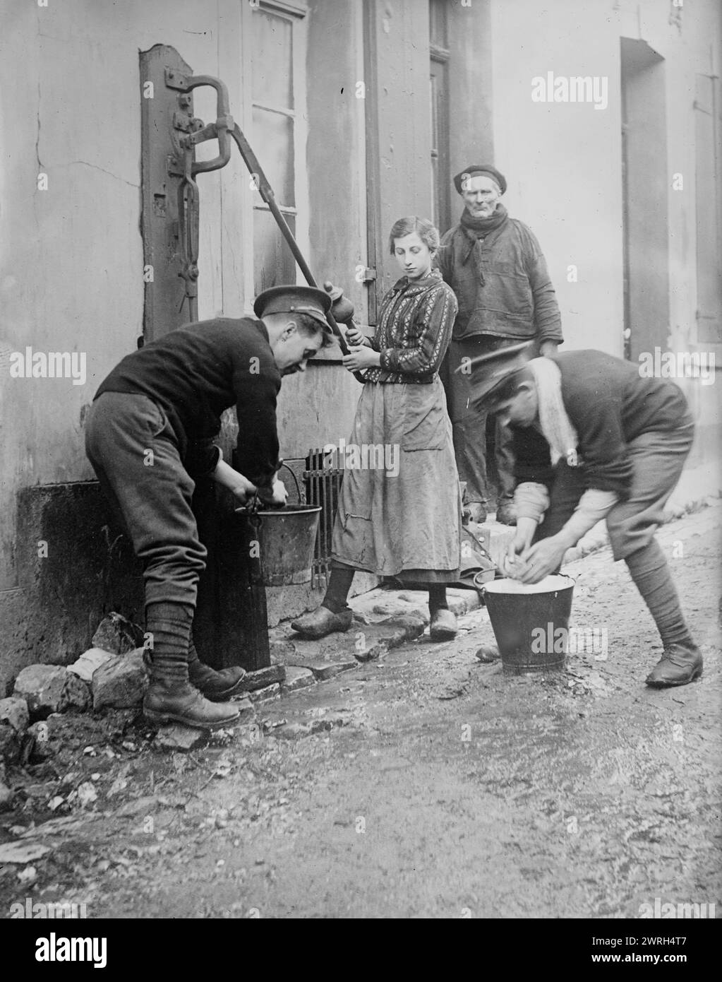 Tommy Atkins at Etaples, between 1914 and c1915. Two British soldiers called &quot;Tommys,&quot; helping some local residents at a water pump, E&#xb4;taples, France, during World War I. Stock Photo