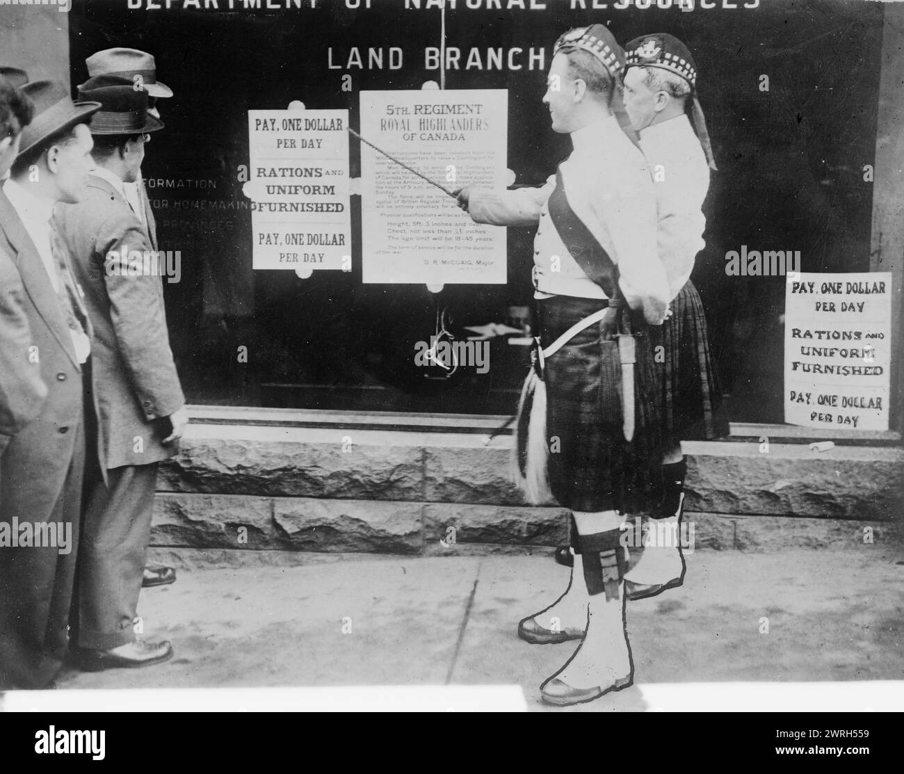 Recruiting, Montreal, 1914 (date created or published later). Soldiers standing in front of a window which displays a recruitment poster for the 5th Regiment Royal Highlanders of Canada, during World War I. Stock Photo