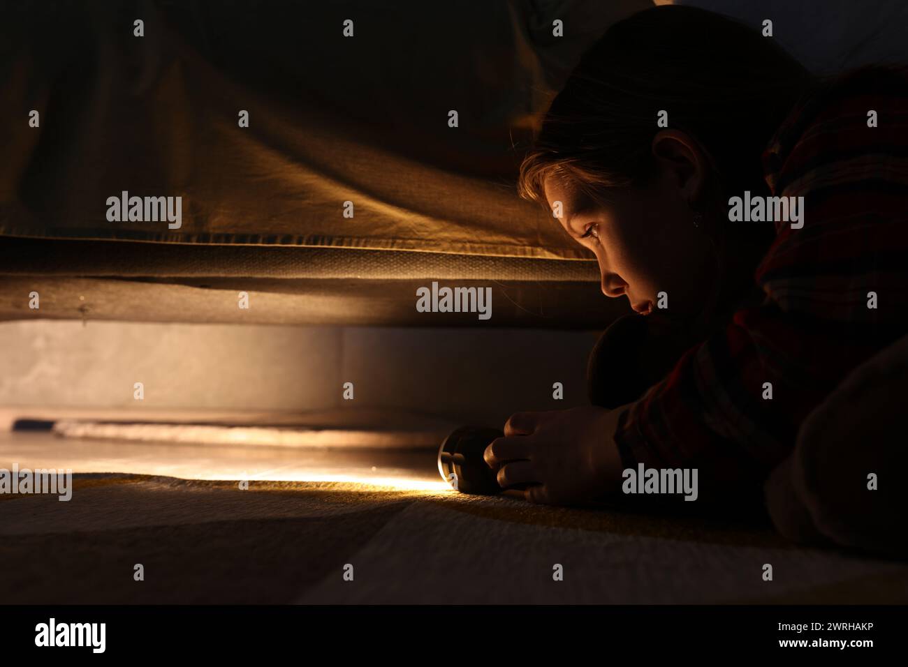 Little girl with flashlight looking for monster under bed at night Stock Photo