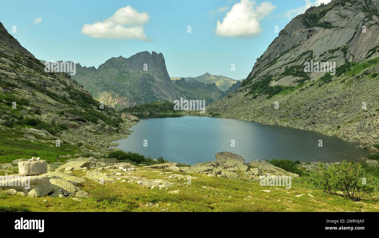 A large picturesque lake with rocky shores at the foot of high steep cliffs on a sunny summer day. Lake of Mountain Spirits, Ergaki Natural Park, Kras Stock Photo