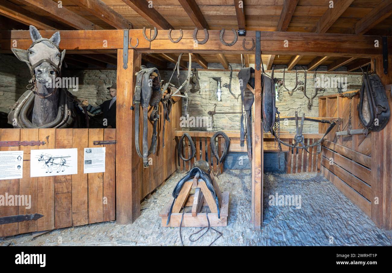 Cromwell, New Zealand - 30 Dec 2023. Inside an old stable at Cromwell Heritage Precinct, with wooden stalls, horse tack, and equestrian equipment. Stock Photo