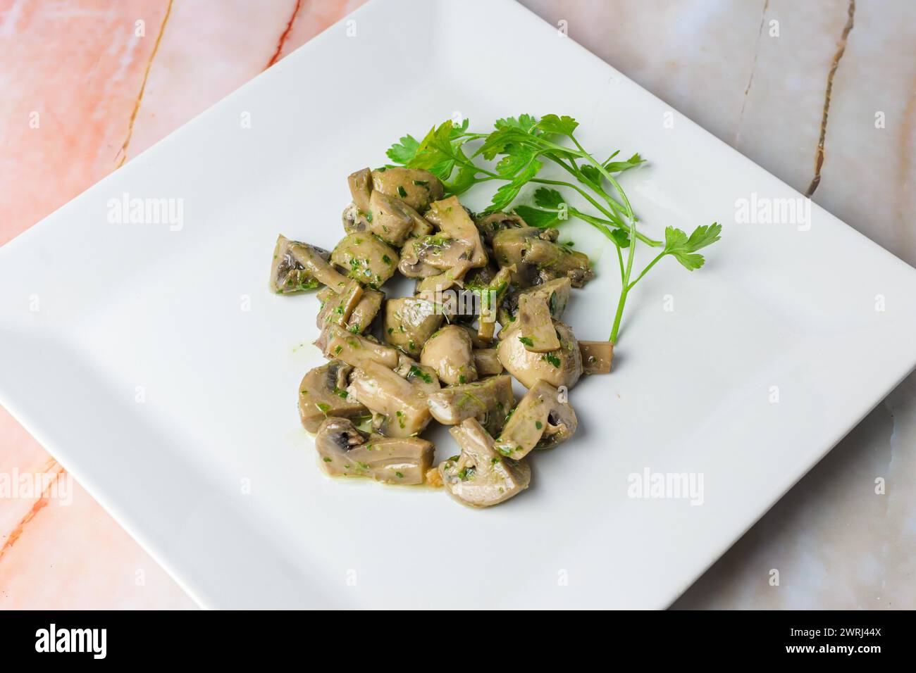 Herb-marinated mushrooms with parsley on a square white plate, typical food, typical mediterranean mallorcan cuisine typical from balearic islands Stock Photo