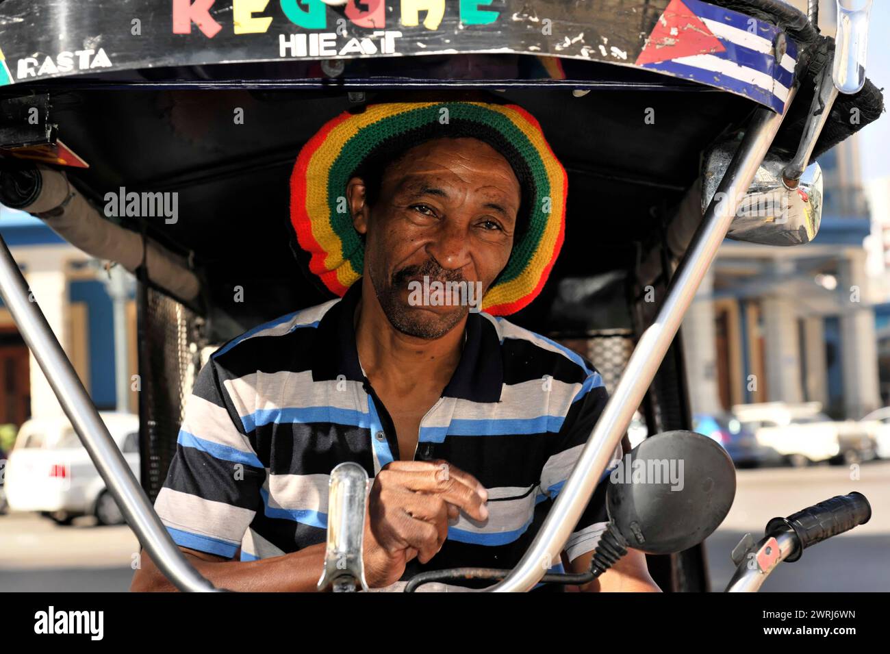 Smiling man with rasta hat driving biker taxi on city street, Havana, Cuba, Central America Stock Photo