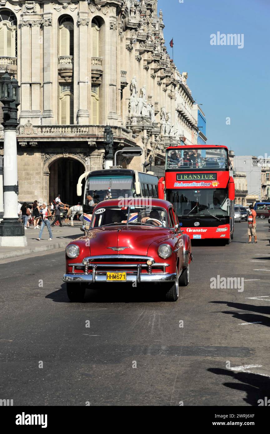 Red vintage car driving on a city street near a red double-decker bus, Havana, Cuba, Central America Stock Photo