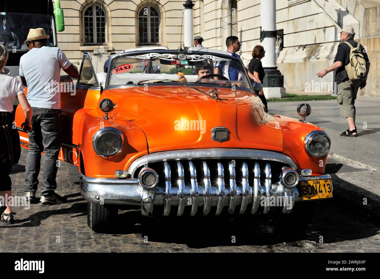 Orange-coloured vintage taxi stops on a lively city street, Havana, Cuba, Central America Stock Photo