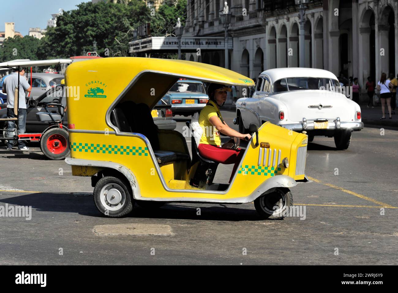 A yellow Tuk Tuk motorbike taxi drives on a city street in Havana, Havana, Cuba, Central America Stock Photo