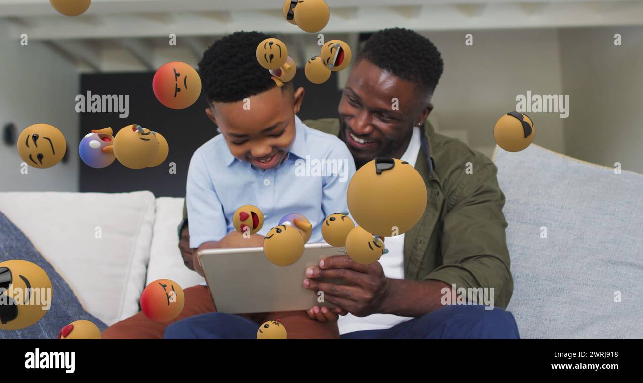 Image of emoticons over happy african american father and son using tablet on sofa Stock Photo