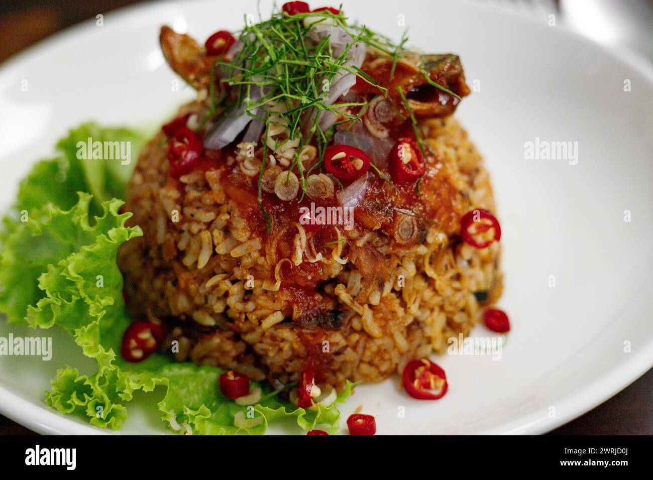 Thai food, Fried jasmine rice with canned fish mackerel in tomato sauce, topped with red chili, red onion, lettuce and kaffir lime leaves. Stock Photo