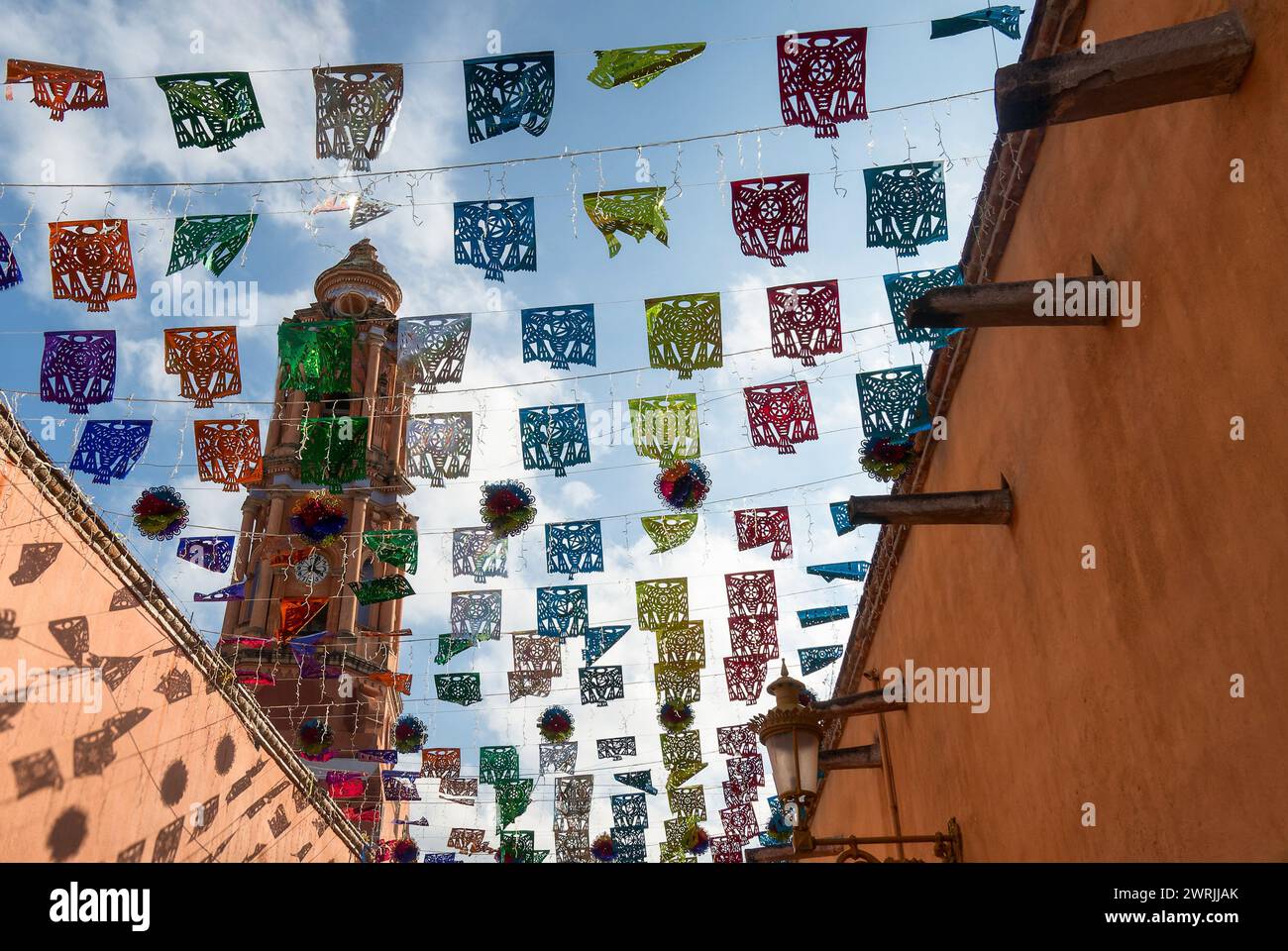 A Mexican street with colorful Papel Picado decorations and a church in the background Stock Photo