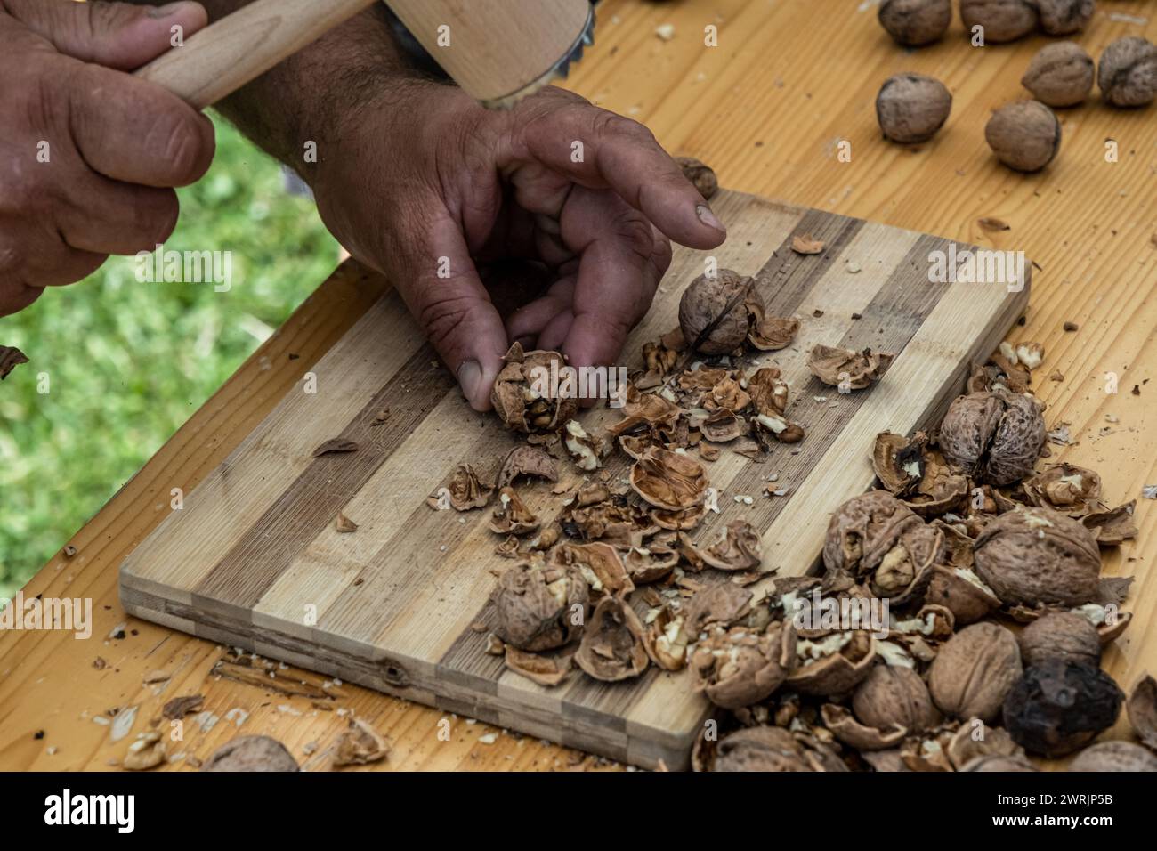 Man cracking walnuts with hammer at table, closeup Stock Photo