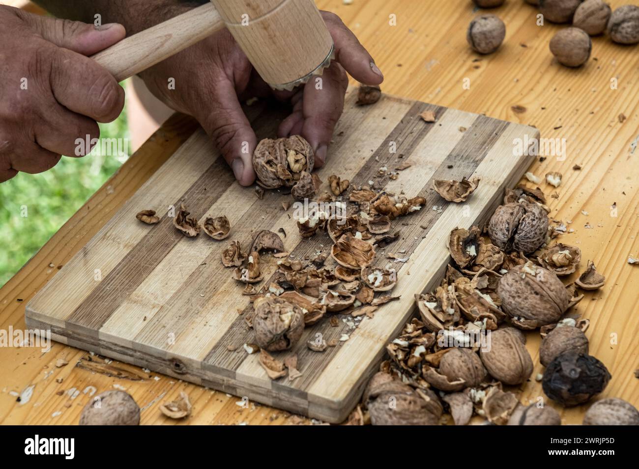 Man cracking walnuts with hammer at table, closeup Stock Photo