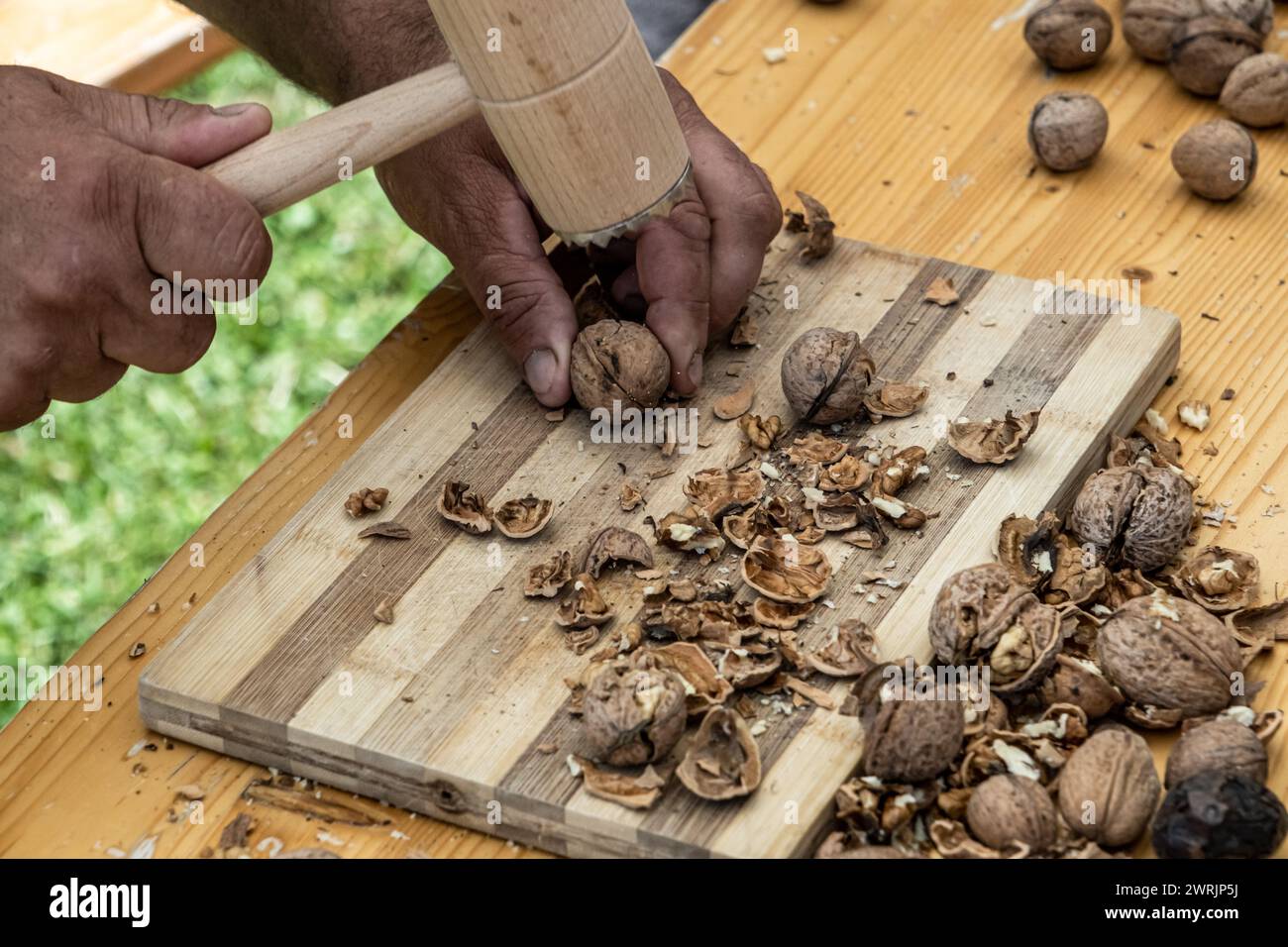 Man cracking walnuts with hammer at table, closeup Stock Photo