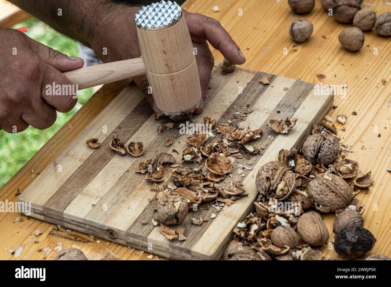 Man cracking walnuts with hammer at table, closeup Stock Photo