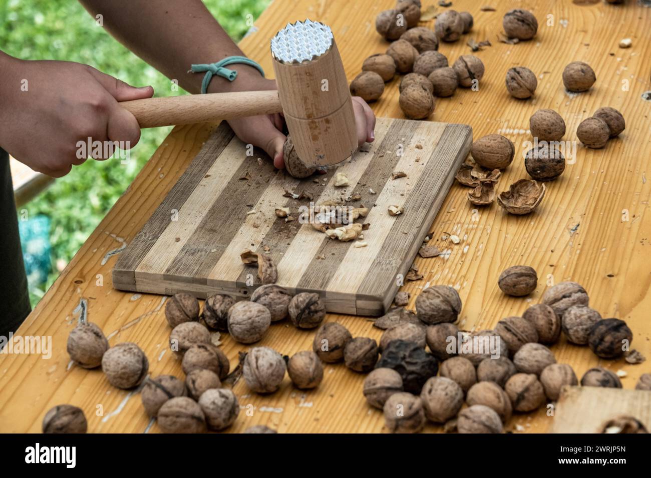 Man cracking walnuts with hammer at table, closeup Stock Photo